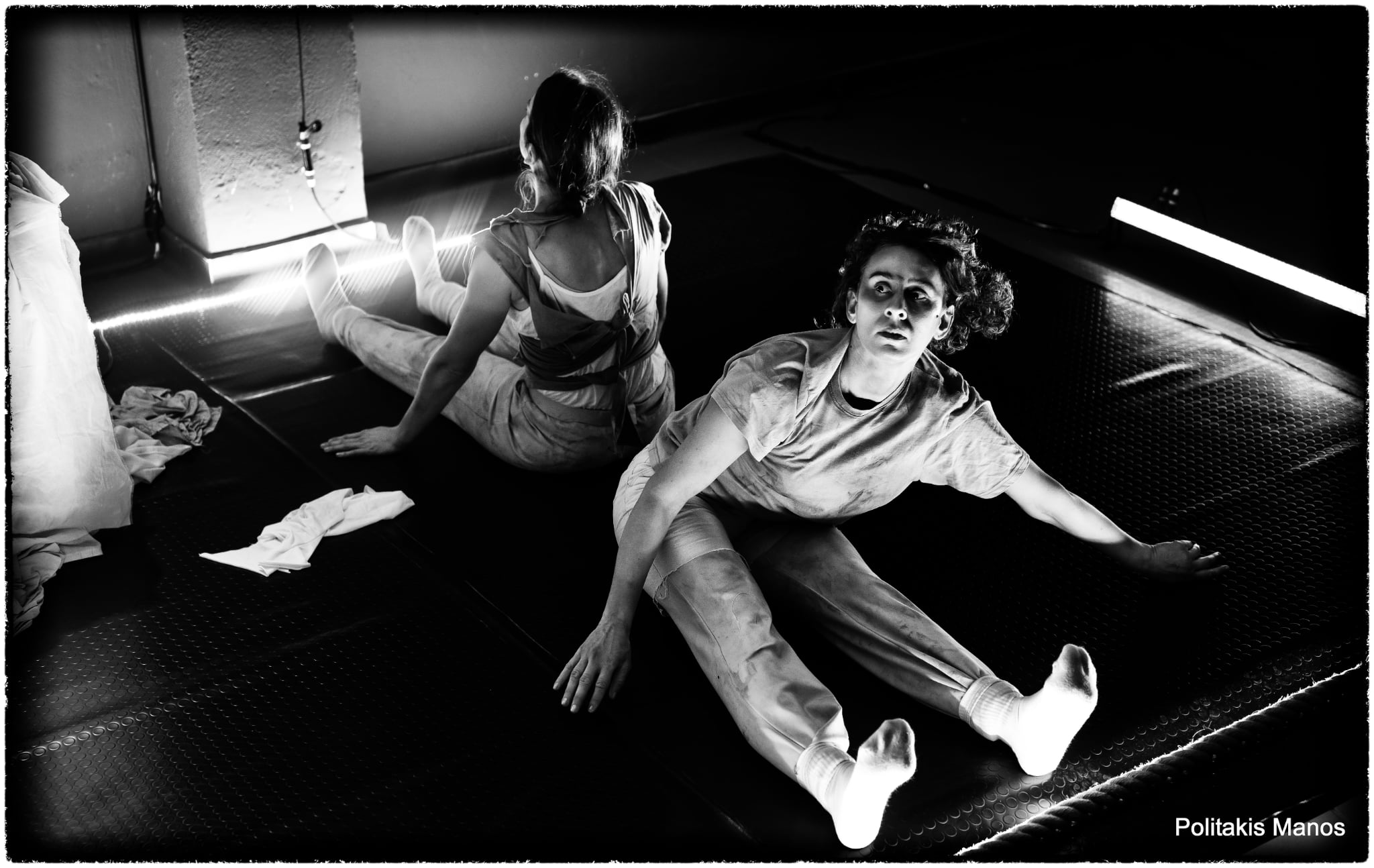 Two performers sit apart on the floor; one turns toward the viewer in Sonderkommando.