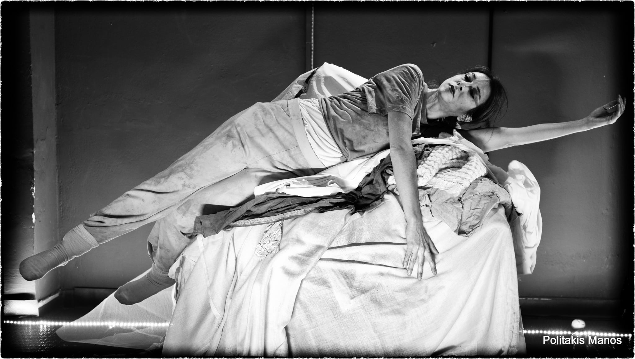 A performer extends one arm while balancing across a mound of fabric in Sonderkommando.